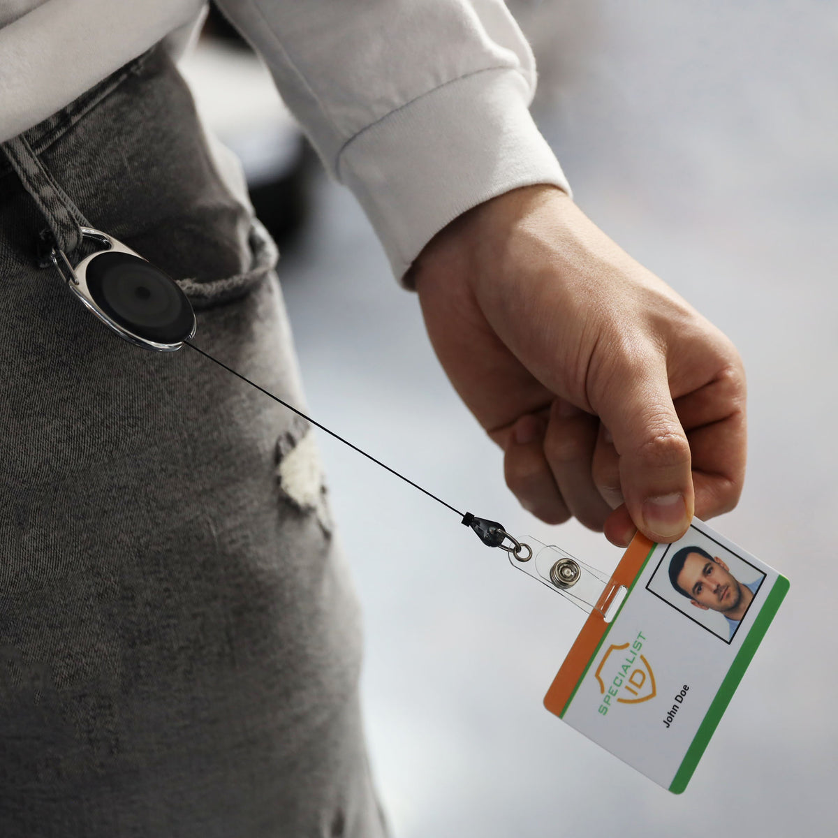 A person in gray pants displays an ID badge using the Carabiner Badge Reel with Oval Clip for Belt Loops and Bag Straps (2120-70XX).