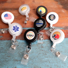 A variety of Custom Badge Reels with Swivel Spring Clip - Personalized Bulk ID Badge Holders for Business, Nurses, and Teachers with colorful designs lay on a wooden surface, perfect for boosting brand awareness at promotional giveaways.