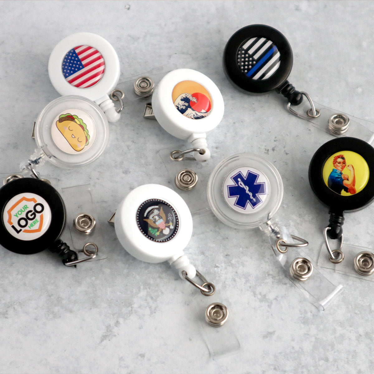 A collection of Custom Badge Reels with Swivel Spring Clip - Personalized Bulk ID Badge Holders for Business, Nurses, and Teachers, each with a different design, including an American flag, taco, medical symbol, and custom logos. Perfect as promotional giveaways for brand awareness, they are arranged on a light grey surface.