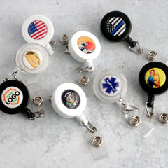 A collection of Custom Badge Reels with Swivel Spring Clip - Personalized Bulk ID Badge Holders for Business, Nurses, and Teachers, each with a different design, including an American flag, taco, medical symbol, and custom logos. Perfect as promotional giveaways for brand awareness, they are arranged on a light grey surface.
