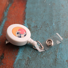 A Custom Badge Reels with Swivel Spring Clip - Personalized Bulk ID Badge Holders for Business, Nurses, and Teachers with a colorful, circular design rests on a worn, teal wooden surface, perfect for brand awareness and promotional giveaways.