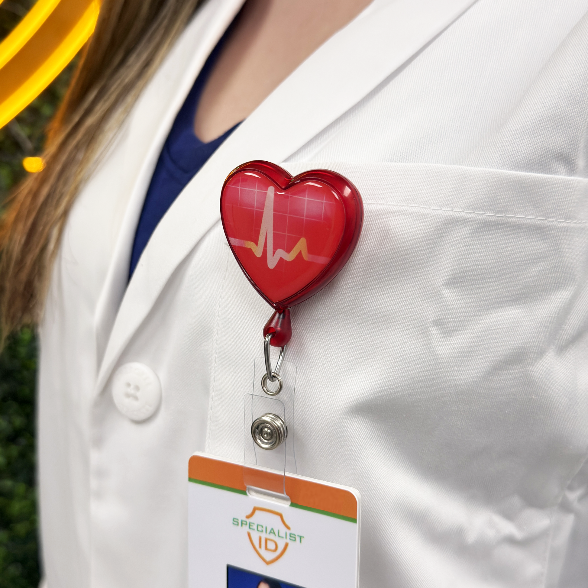 Person wearing a white lab coat with a red heart-shaped badge holder that has an EKG line design and 'Specialist ID' card attached to the vinyl ID strap