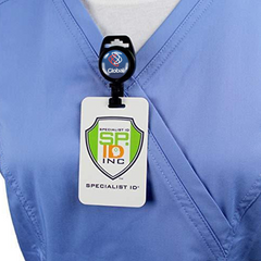 A person wearing a blue scrub top with a name badge clipped on the chest. The badge, attached to a Custom Non-Magnetic Badge Reel with Plastic Clip - No Twist Design - Add Your Logo, displays "SP 10 INC" and "SPECIALIST ID" text under a shield logo.