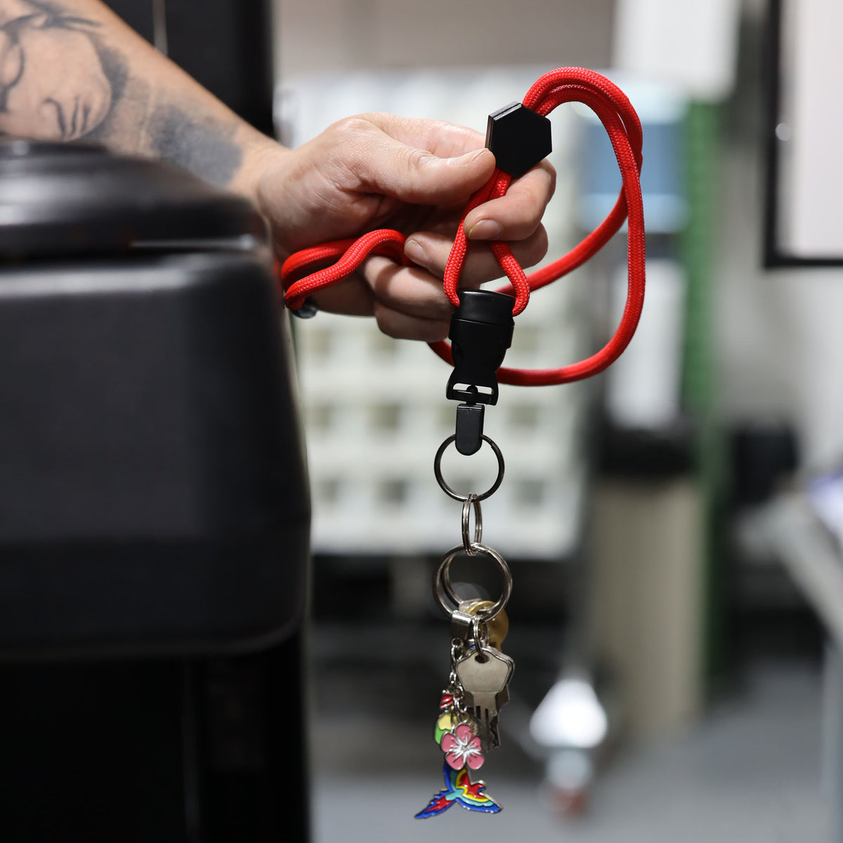 A hand holds a Heavy Duty Breakaway Round Lanyard With Detachable Key Ring (2135-454X) in red, custom printed and featuring several keys and a colorful boot-shaped keychain adorned with a flower.