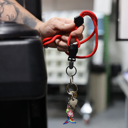 A hand holds a Heavy Duty Breakaway Round Lanyard With Detachable Key Ring (2135-454X) in red, custom printed and featuring several keys and a colorful boot-shaped keychain adorned with a flower.