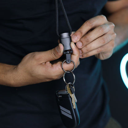 A person wearing a black shirt holds the 1/4″ Breakaway Round Lanyard with Detachable Split Ring (2135-461X), which has keys and a key fob attached.