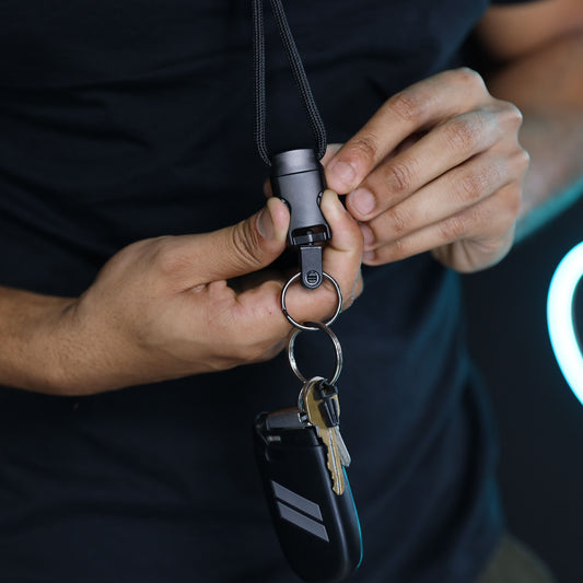 A person wearing a black shirt holds the 1/4″ Breakaway Round Lanyard with Detachable Split Ring (2135-461X), which has keys and a key fob attached.