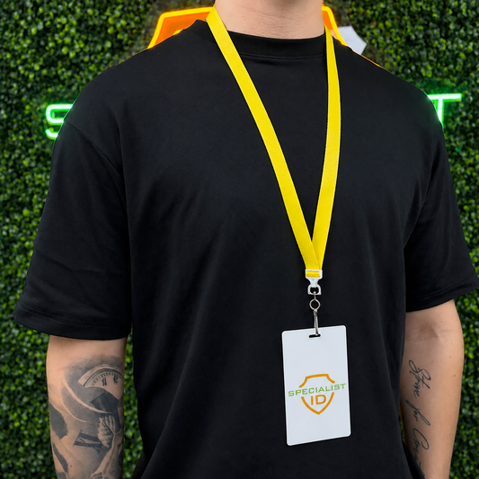 A person in a black t-shirt wears a yellow Flat Wide Breakaway Lanyard with Swivel Hook - 5/8 Inch Width (2138-500X) and Specialist ID badge, standing before green leafy decor and a neon sign.