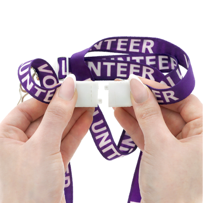 Purple 'VOLUNTEER' lanyard held by hands against a white background. Featured breakaway clasp shown detached. Sold by Specialist ID.