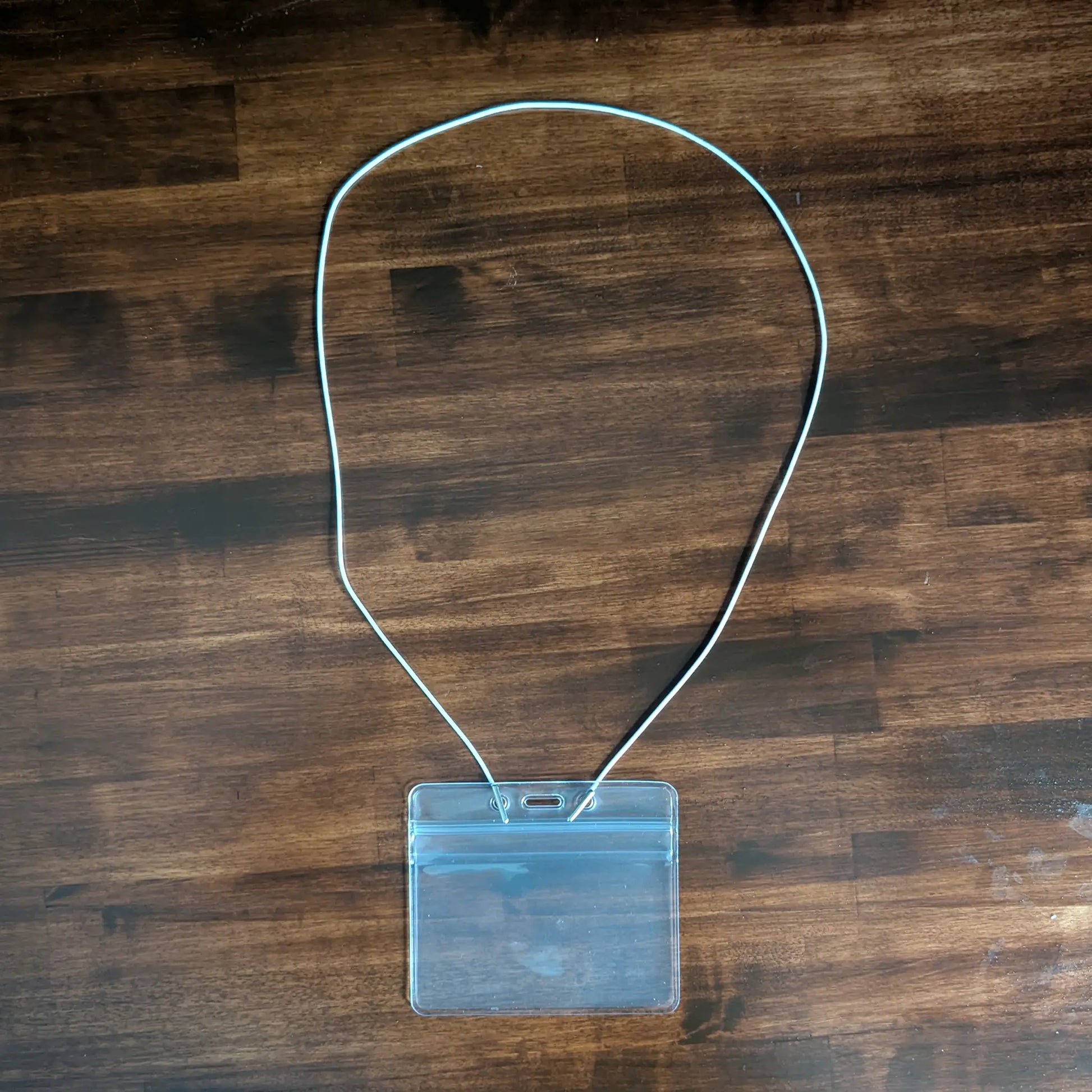 The Elastic No-Twist Neck Cord for ID Event Badge Holders (2140-15XX Series) securely holds a clear plastic badge holder, shown neatly displayed on a wooden surface.