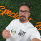 A man with glasses and a beard holds up an SPiD badge attached to an Elastic No-Twist Neck Cord for ID Event Badge Holders (2140-15XX Series) while standing in front of a green wall with orange cursive writing.