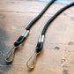 Close up of two black braided rope lanyards with metal hooks on a wooden surface