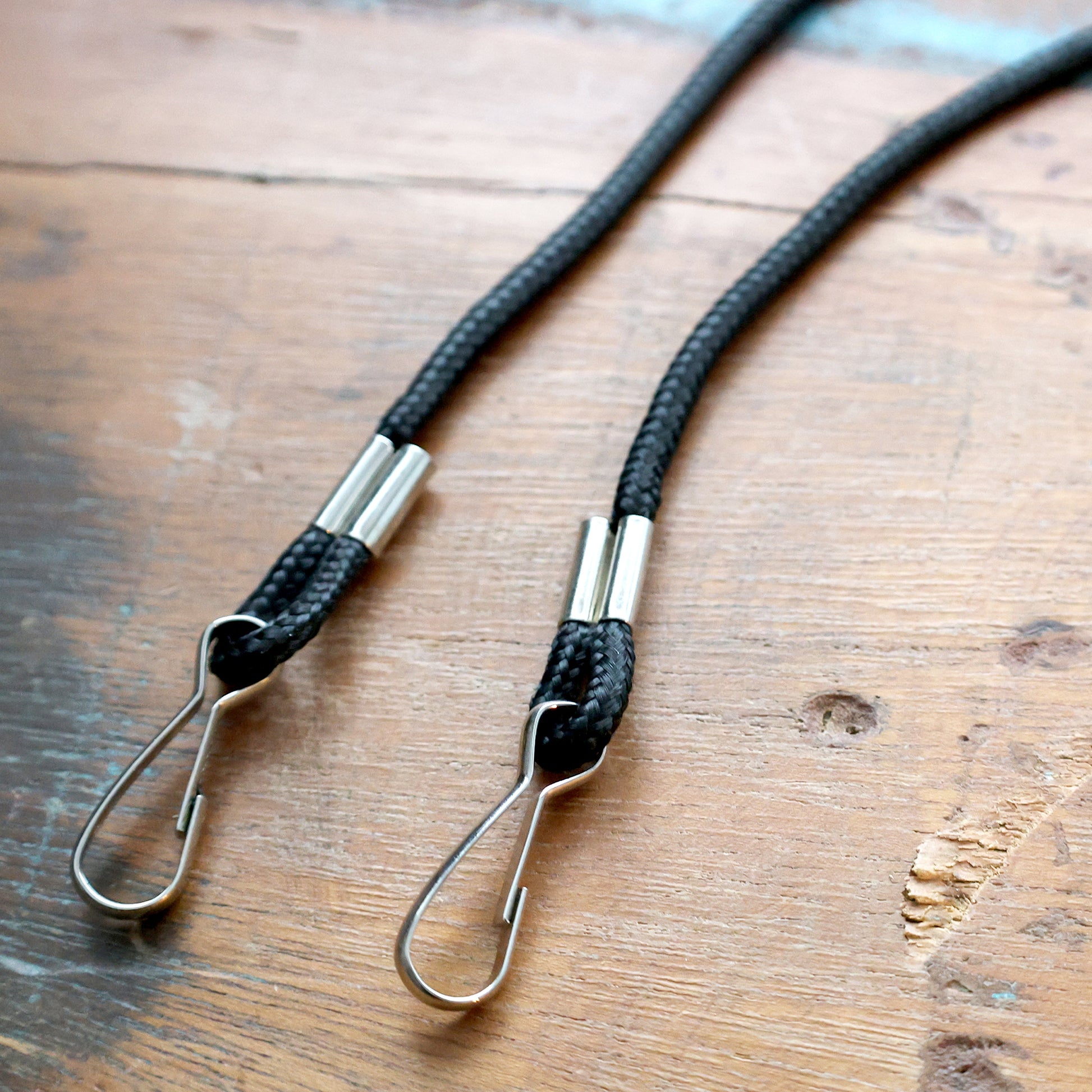 Close up of two black braided rope lanyards with metal hooks on a wooden surface