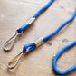 Close-up of the Round Special Event Blue Rope Lanyard with Two Clips 2140-5802 on a wooden surface, featuring a blue braided cord, metal looped ends, and cylindrical connectors—ideal as a double clip ID badge holder. 