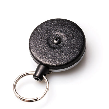 A Key-Bak #485B-HDK Self Retracting Key Reel with a textured surface and a Kevlar cord for durability, featuring a keyring attached to its side.