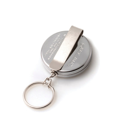 A round, metallic **Key-Bak #5 Self Retracting Key Badge Reel** with an attached keyring and a belt clip, featuring a self-retracting key reel and a sturdy Kevlar cord.