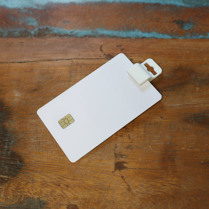 A white Gripper 30 Card Clamp (P/N 5710-3058) is used to securely hold a plastic card with a chip on the wooden table. Sold by Specialist ID.