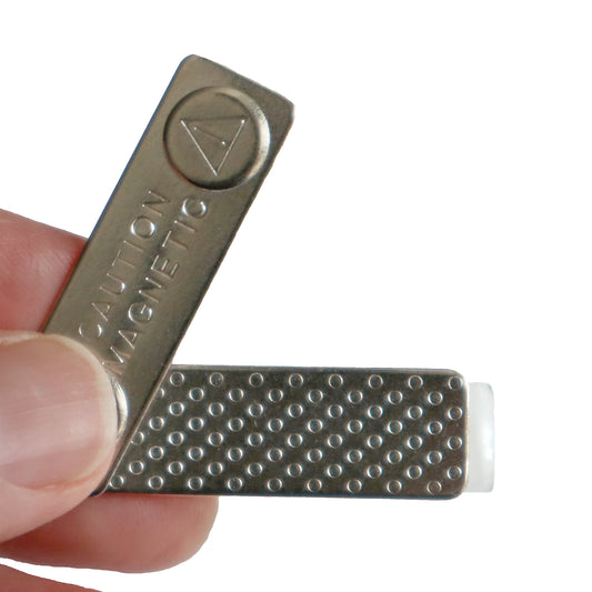 A hand holding a metal tool inscribed with "CAUTION MAGNETIC," showing a textured surface and a white tip, resembling the attention to detail found in a Magnetic ID Badge Holder Sticky Back (P/N 5730-3000).