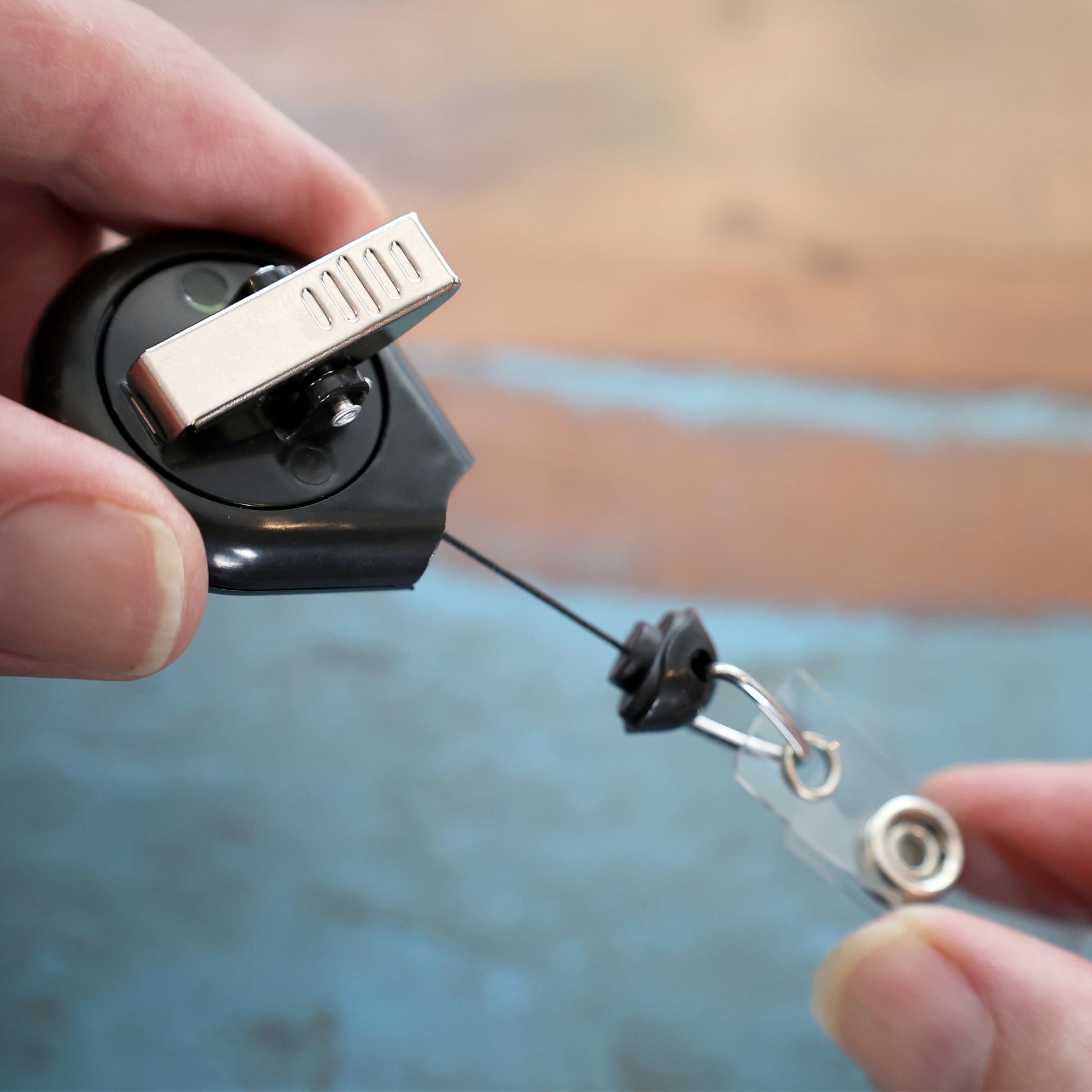 A hand is holding the Premium No Twist Badge Reel with Swivel Spring Clip - Teardrop Shape (609-I-BLK), extending its retractable cord to reveal the attached badge holder.