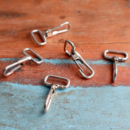 Five 1 3/4" Non Swivel J Hook with Rectangular End - DIY Lanyard and Craft Accessories (6920-2400) lie scattered on a distressed, two-toned wooden surface, combining reddish-brown and light blue hues.