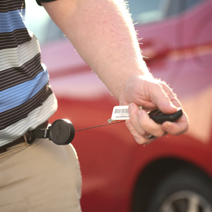 A person holds a Key-Bak Mid Size Carabiner Badge Reel with Key Ring (6C) attached to their belt loop, standing in front of a red car.