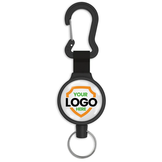 A Customizable Key-Bak 6C Carabiner Badge Reel - Retractable Keychain Reel with 36" Cord and Easy Logo Upload with a carabiner clip at the top and a key ring at the bottom. The central circular area displays a custom logo placeholder with the text "YOUR LOGO HERE." Perfect for promoting brand awareness, this retractable holder is both functional and personalized.