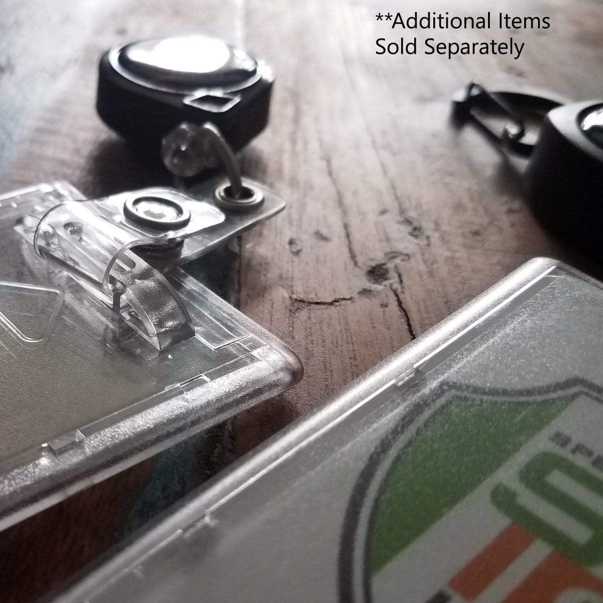 Close-up of Premium Top Load Slim Rigid Plastic ID Badge Holder with Easy Access Thumb Slide Removal (706-N) and retractable badge reels on a wooden surface. Text reads: "**Additional Items Sold Separately." Ideal for credit card sized ID badges.
