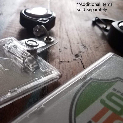 Close-up of Premium Top Load Slim Rigid Plastic ID Badge Holder with Easy Access Thumb Slide Removal (706-N) and retractable badge reels on a wooden surface. Text reads: "**Additional Items Sold Separately." Ideal for credit card sized ID badges.