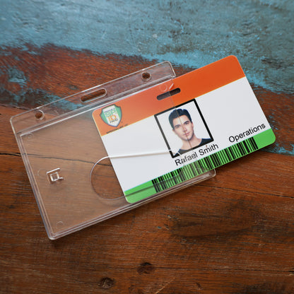 An employee ID card labeled “Rafael Smith, Operations” is partially out of a Horizontal Economy Crystal Clear Card Dispenser (P/N 726-CT1) with a thumb notch, resting on a wooden surface.