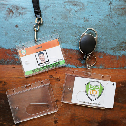 A Horizontal Economy Crystal Clear Card Dispenser and a green Specialist ID card, along with a retractable badge reel and a photo ID labeled Rafael Smith, are shown on a wooden surface.