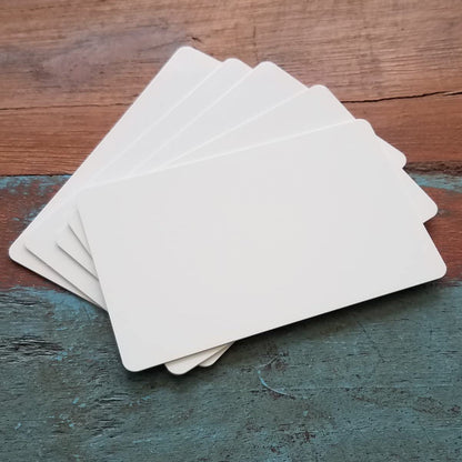 A stack of blank, white 500 Pack - Standard CR80 30mil Composite PVC/Poly Cards lies fanned out on a wooden surface—perfect for company IDs or use with ID card printers. old by Specialist ID. 