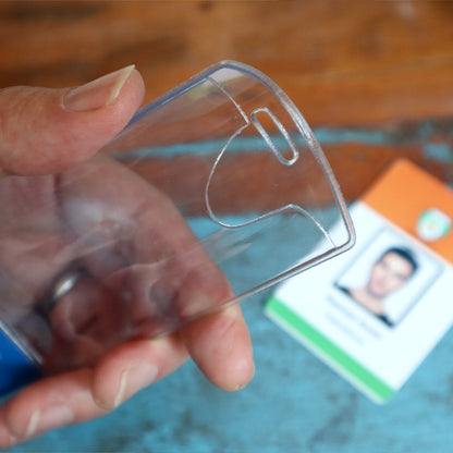 A hand displays the NURSE PRACTITIONER BadgeBottom, a vertical ID badge holder with a role tag, exemplifying its simplicity and elegance on a table with an ID card visible in the background. Made from durable composite material, it's ideal for professionals like Nurse Practitioners.