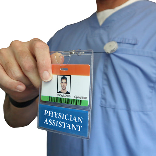 A person in blue scrubs holds up a PHYSICIAN ASSISTANT BadgeBottom Badge Holder & PHYSICIAN ASSISTANT Badge Buddy—a horizontal ID badge sleeve featuring a bottom role tag for Physician Assistants.