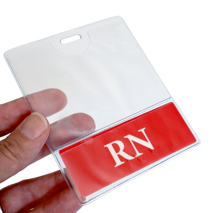 A person's hand holding a clear plastic RN BadgeBottom Badge Holder & RN Badge Buddy IN ONE!! - Horizontal ID Badge Sleeve with Bottom Role Tag for Registered Nurses with a red label that has the letters "RN" in white.