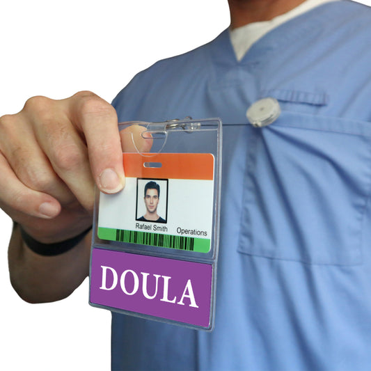 A person in scrubs wears a DOULA BadgeBottom Badge Holder & DOULA Badge Buddy, featuring a horizontal ID badge sleeve with a bottom role tag labeled "DOULA," including their photo and name.