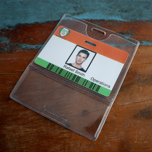 A plastic ID badge with a photo of a person, labeled "Rafael Smith" and "Operations," placed on a wooden surface, enclosed in a Premium Vinyl Horizontal BadgeBottom with Slot - Holder Only.