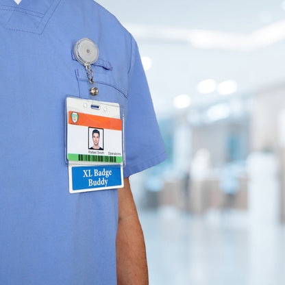 Close-up of a person wearing blue scrubs with a visible badge holder displaying an ID card labeled "Rahul Singh, Operations" and another card labeled "Oversized LPN Badge Buddy - XL Badge Backer for Nurses - Horizontal Hospital ID Badge Buddies." This licensed practical nurse is part of our dedicated team in various healthcare settings. Background is blurred.