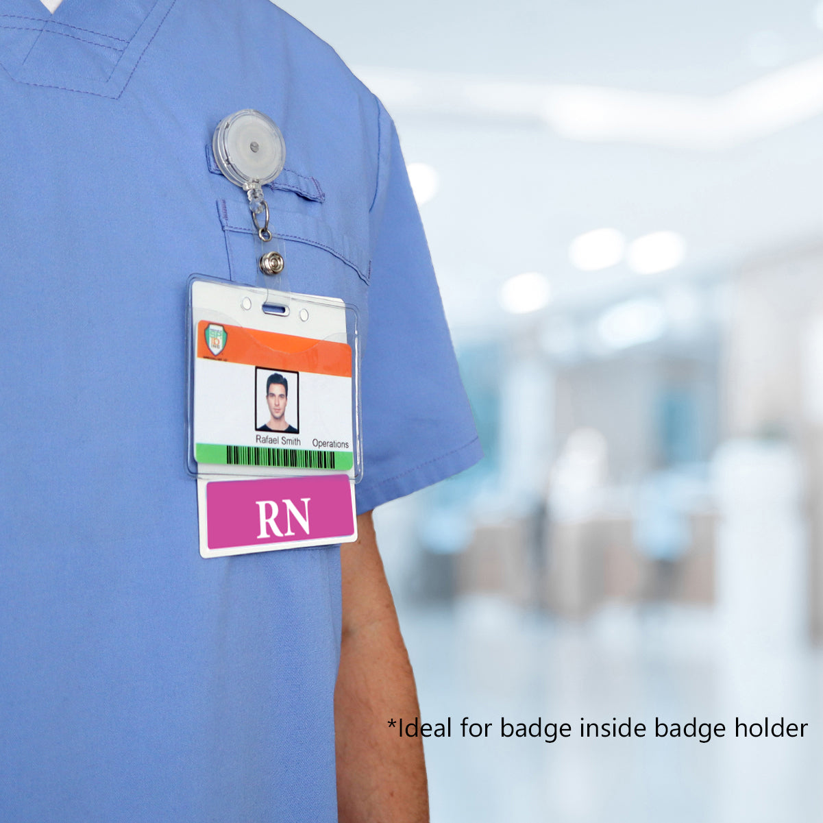 Close-up of a person wearing blue scrubs with an Extra Large RN Badge Buddy - XL Badge Backer for Registered Nurse - Horizontal Hospital ID Badge Buddies attached to the chest pocket. The horizontal hospital ID includes a photo, name, role, and an additional RN label. Background is blurred indoors.