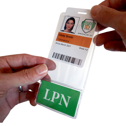 Person holding a clear plastic badge holder with an ID card inside. The ID card has a photo, name "Cindy Smith," title "Operations," and indicates it has been valid since March 2021. The LPN BadgeBottom Badge Holder & Badge Buddy IN ONE!! - Vertical ID Badge Sleeve with Bottom Role Tag for Nurses shows "LPN.