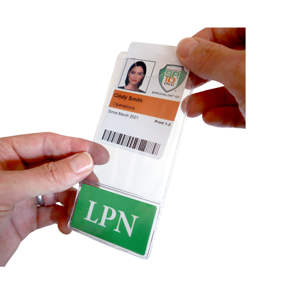 A person holds an ID badge featuring a customizable LPN BadgeBottom Badge Holder & Badge Buddy IN ONE!! - Vertical ID Badge Sleeve with Bottom Role Tag for Nurses that reads "Cindy Smith, Operations, Since March 2021" with a green "LPN" label at the bottom.