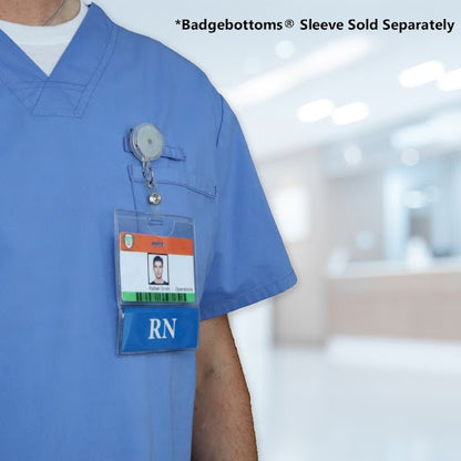 A person in a blue medical uniform with an RN badge holder containing an ID card and a pen, standing in a blurred hospital setting, showcases Horizontal Custom BadgeBottoms Insert Only (Holder Not Included) - Add Your Unique Title perfect for the dynamic medical workplace.