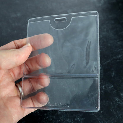 A hand holds a Custom Printed BadgeBottoms® Horizontal (Badge Holder & Badge Buddy IN ONE) against a dark background, showcasing its sleek design suitable for customizable titles. Sold by Specialist ID.