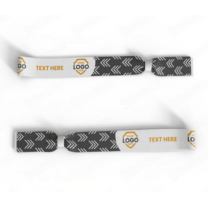 The Custom Printed Wristband features black and white dye-sublimated arrow patterns, customizable logo areas, and a "TEXT HERE" section for personalized messages—perfect as event wristbands or unique accessories.