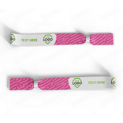 Two Custom Printed Wristbands with pink patterned ends, a logo placeholder, and green "TEXT HERE" text are shown on a white background. Sold by Specialist ID.