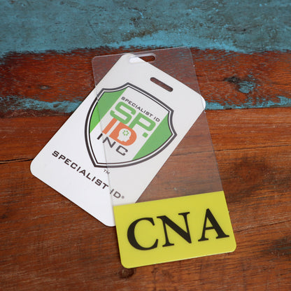 Two identification badges on a wooden surface. One badge features a logo with "Specialist ID SP Inc." and the other reads "CNA" with a yellow bottom section, serving as a clear Clear CNA Badge Buddy Vertical with Yellow Border for Nursing Assistants.