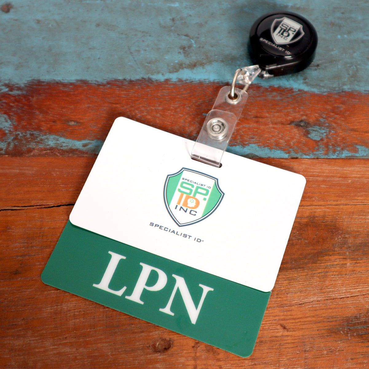 A green and white ID badge with the initials "LPN" and a clear LPN Badge Buddy - Horizontal ID Badge Backer for Licensed Practical Nurses - Double Sided Print lies on a distressed wooden surface, ideal for licensed practical nurses in a healthcare setting.