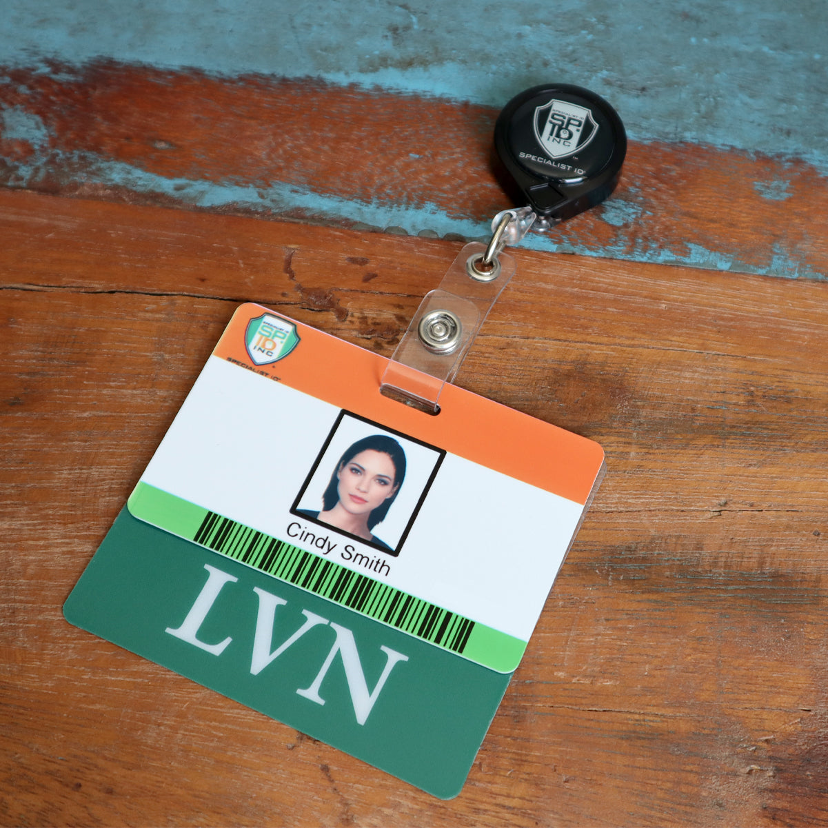 A name badge with a retractable clip shows an ID card labeled "Cindy Smith" and marked "LVN." The card features a photo of a woman and is accompanied by a Clear LVN Badge Buddy - Horizontal ID Badge Backer for Licensed Vocational Nurses - Double Sided Print, set against a wooden and blue background.