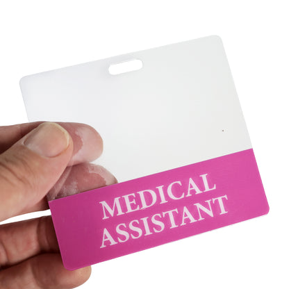 A hand holds the Clear MEDICAL ASSISTANT Badge Buddy, a horizontal nurse ID badge backer with double-sided print and a pink section labeled "MEDICAL ASSISTANT" for clear role recognition.