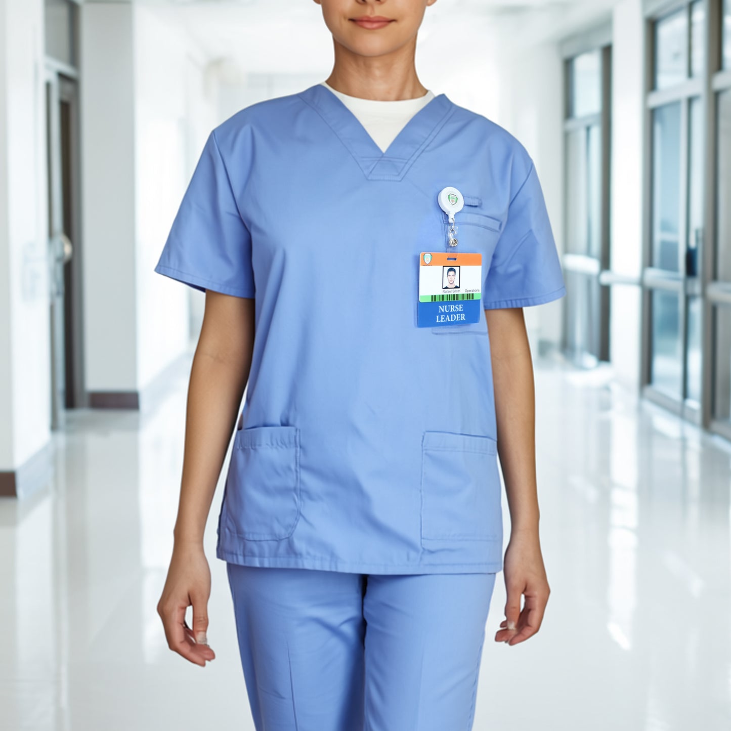 A person in light blue scrubs wears the Clear NURSE LEADER Badge Buddy—Horizontal Nurse ID Badge Backer, Double Sided Print—while standing in a bright hallway with glass doors and windows.