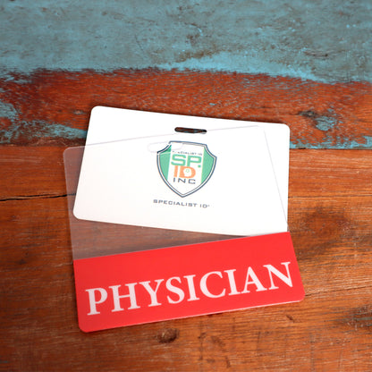 A Clear PHYSICIAN Badge Buddy - Horizontal ID Badge Backer for Physicians - Double Sided Print is placed on a wooden surface with a blue and brown background. Sold by Specialist ID.